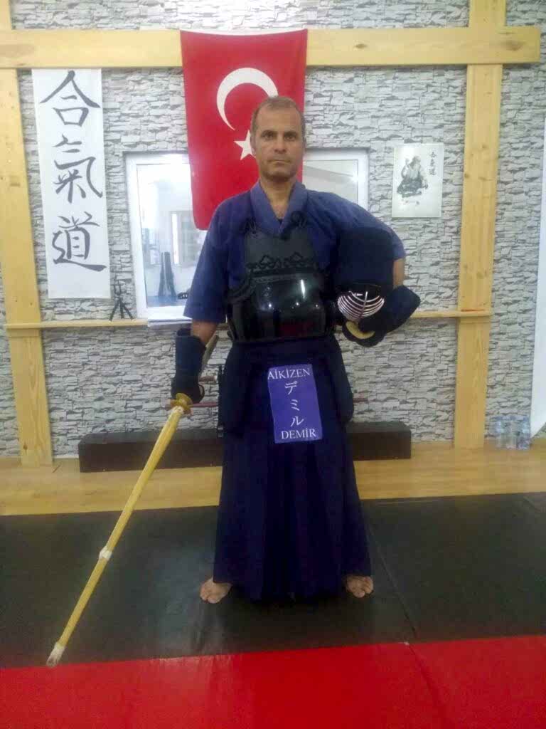 Kürşat Demir, geleneksel Kendo giysisi (keikogi ve hakama) ve zırhı (bogu) ile bir shinai tutarken bir dojo'da poz veriyor.