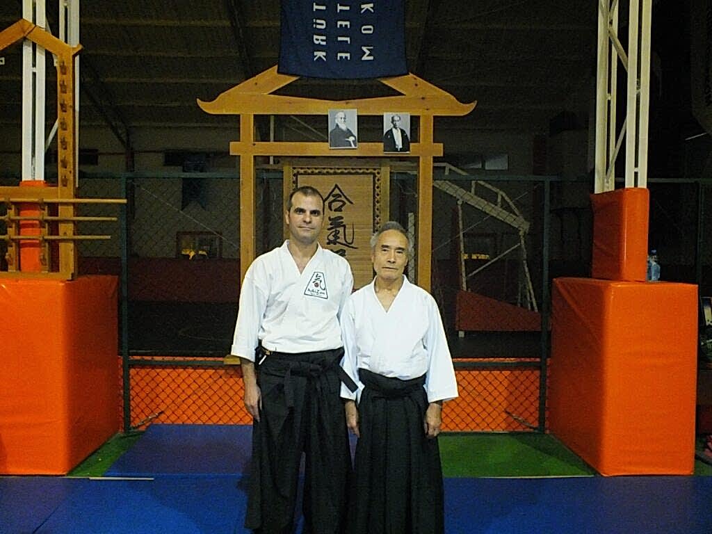 Kürşat Demir, dojo kapısı önünde Sensei Takeo Santsumi  ile geleneksel beyaz giysiler içinde yan yana ayakta duruyor.